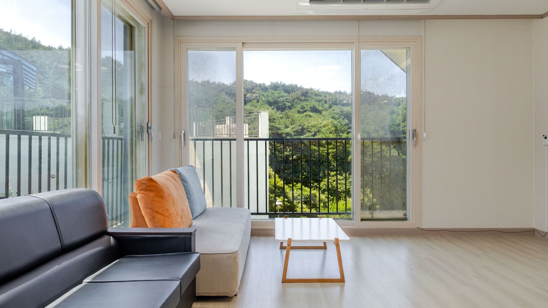 A modern living room with a sofa, a coffee table, and a balcony with a view of a forested area.