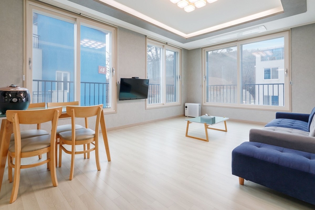 A modern living room with a sofa, wooden chairs, a small table, and a TV mounted on the wall.