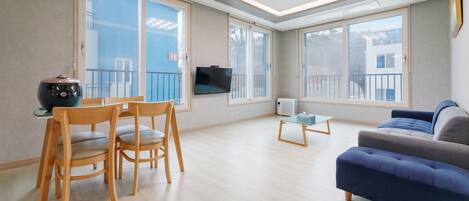 A modern living room with a sofa, wooden chairs, a small table, and a TV mounted on the wall.