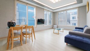 A modern living room with a sofa, wooden chairs, a small table, and a TV mounted on the wall. - Taean Blueisland Pool Villa (Taean)