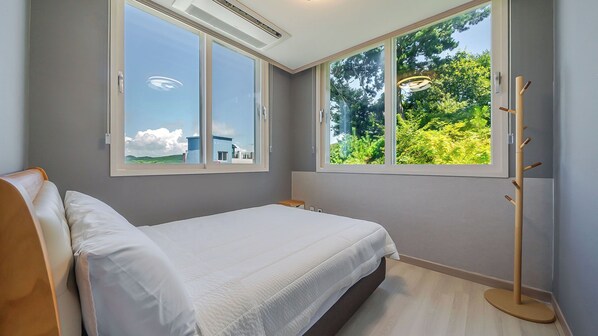 A bedroom with a bed, a bedside table, a window with a view of greenery, and a coat rack.