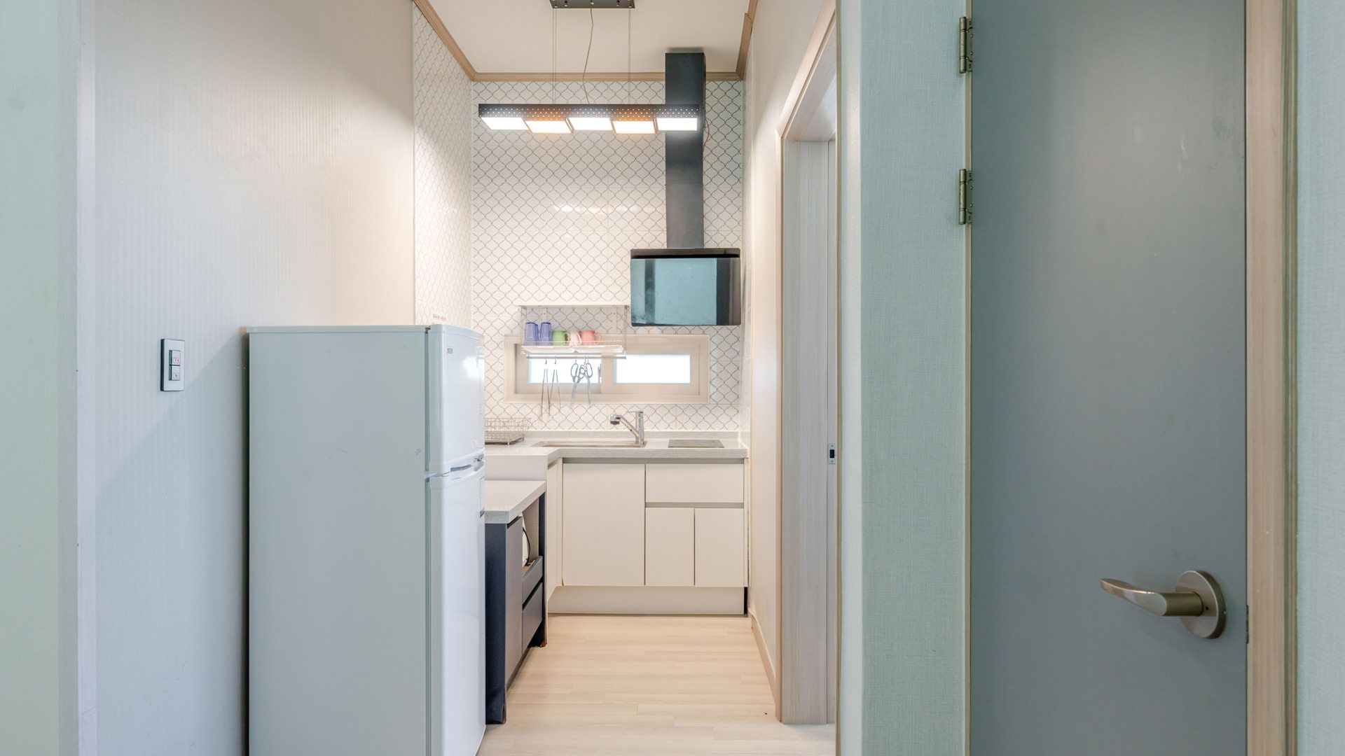 A narrow hallway leading to a kitchen with a refrigerator, sink, and a microwave.