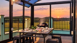 A dining area with a table set for a meal, a grill, and a scenic view of the sunset. - Taean Blueisland Pool Villa (Taean)