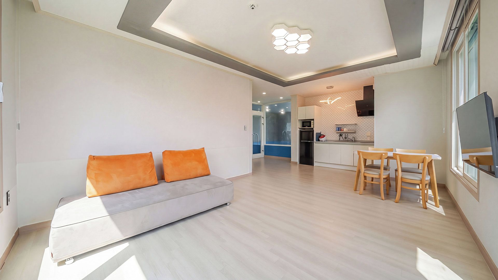 Una sala de estar moderna con un sofá y cojines naranja, un comedor con mesa y sillas, y una cocina al fondo.