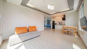 A modern living room with a sofa and orange cushions, a dining area with a table and chairs, and a kitchen in the background. - Taean Blueisland Pool Villa (Taean)