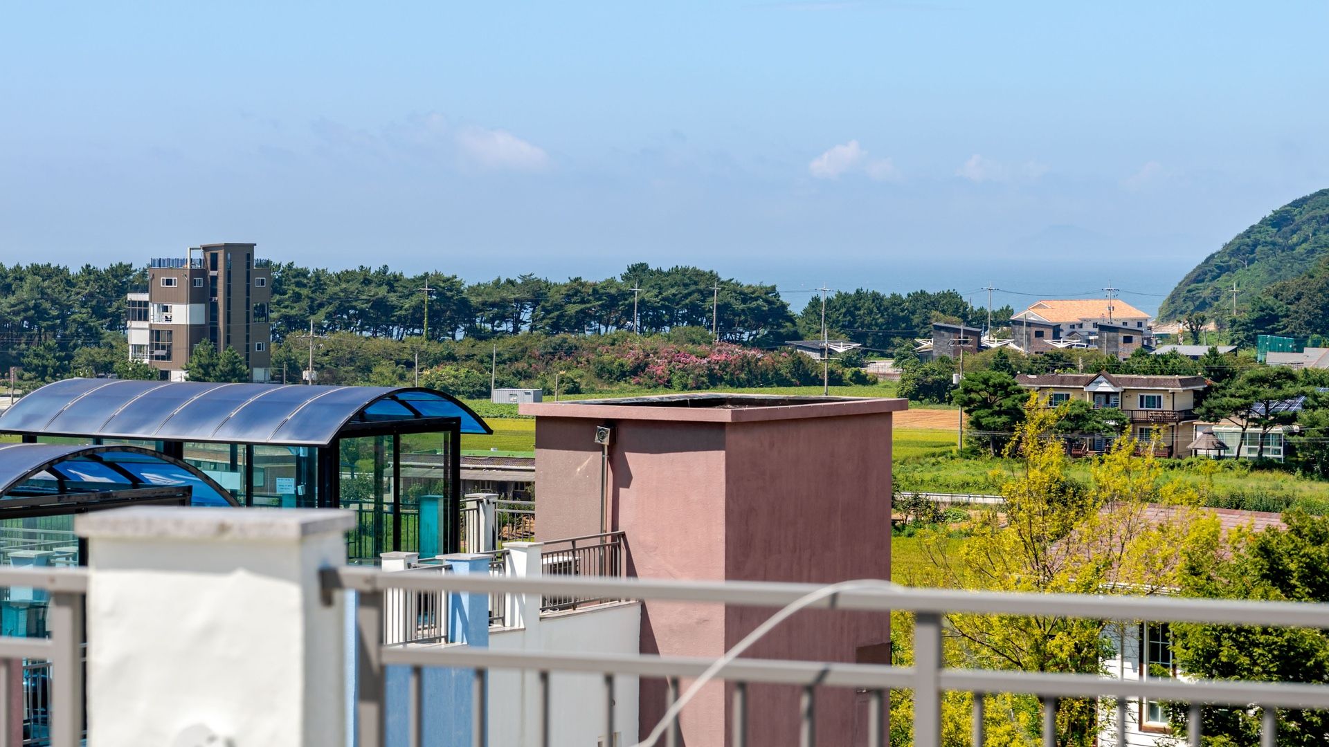 A residential area with modern buildings, a clear sky, and a view of the sea.