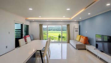 Una sala de estar moderna con comedor, televisor de pantalla plana y vista a un paisaje verde.