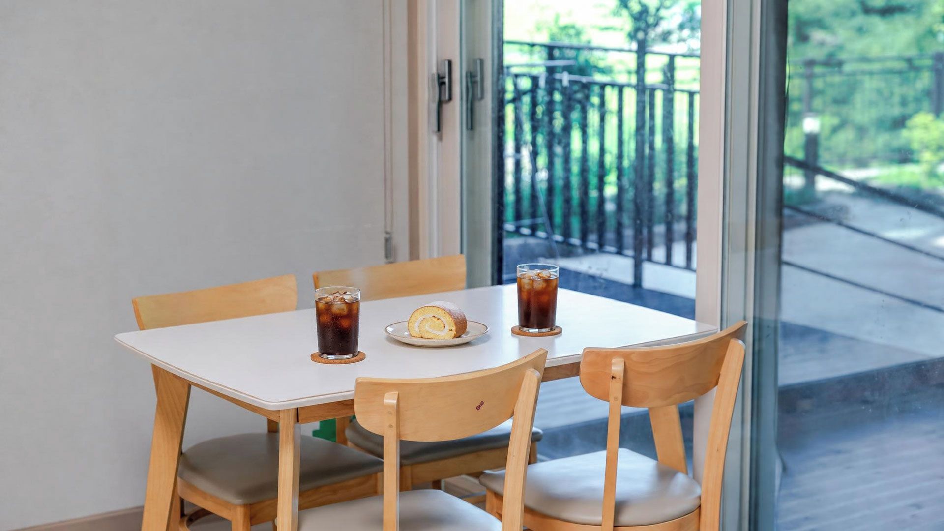Een tafel met een bord eten en twee drankjes, houten stoelen en uitzicht op een balkon met een leuning.