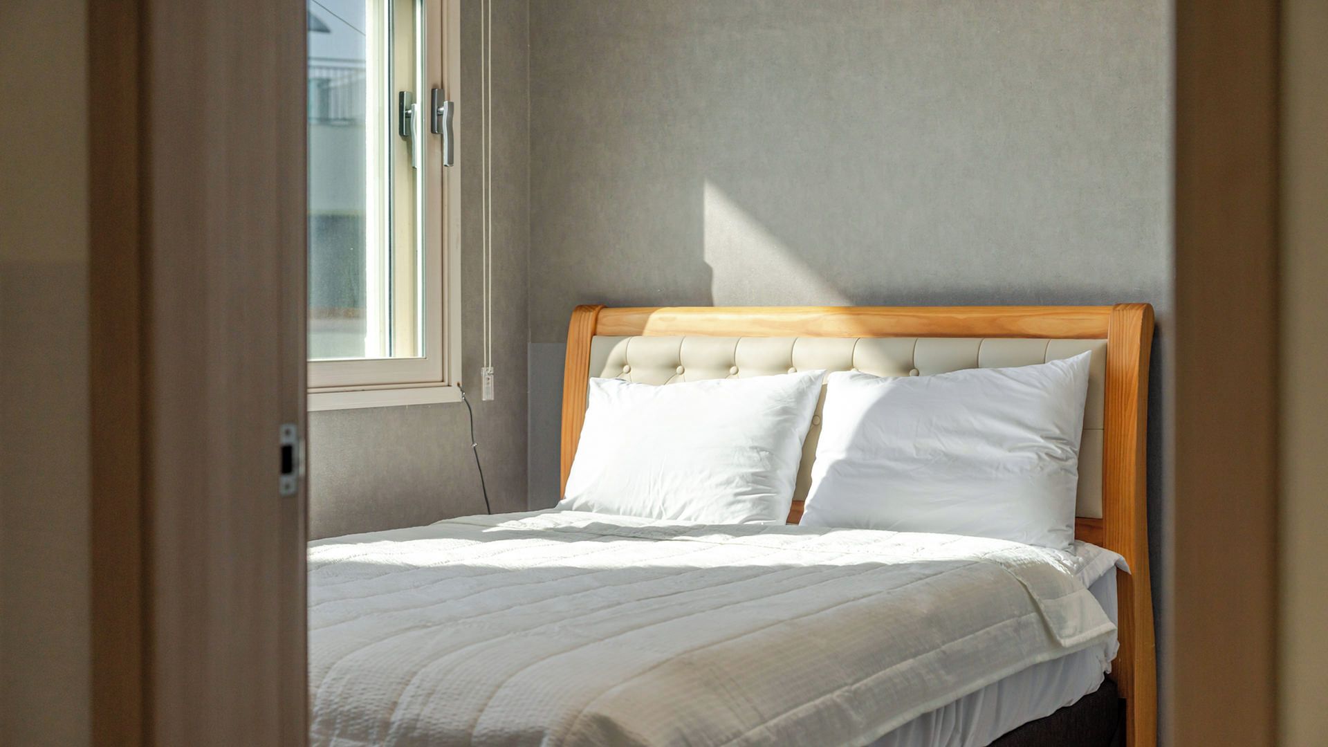 Ein ordentlich bezogenes Bett mit hölzernem Kopfteil und weißer Bettwäsche in einem Zimmer mit einem Fenster.