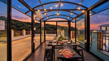 An outdoor dining area with a grill, tables, and chairs, overlooking a scenic landscape.