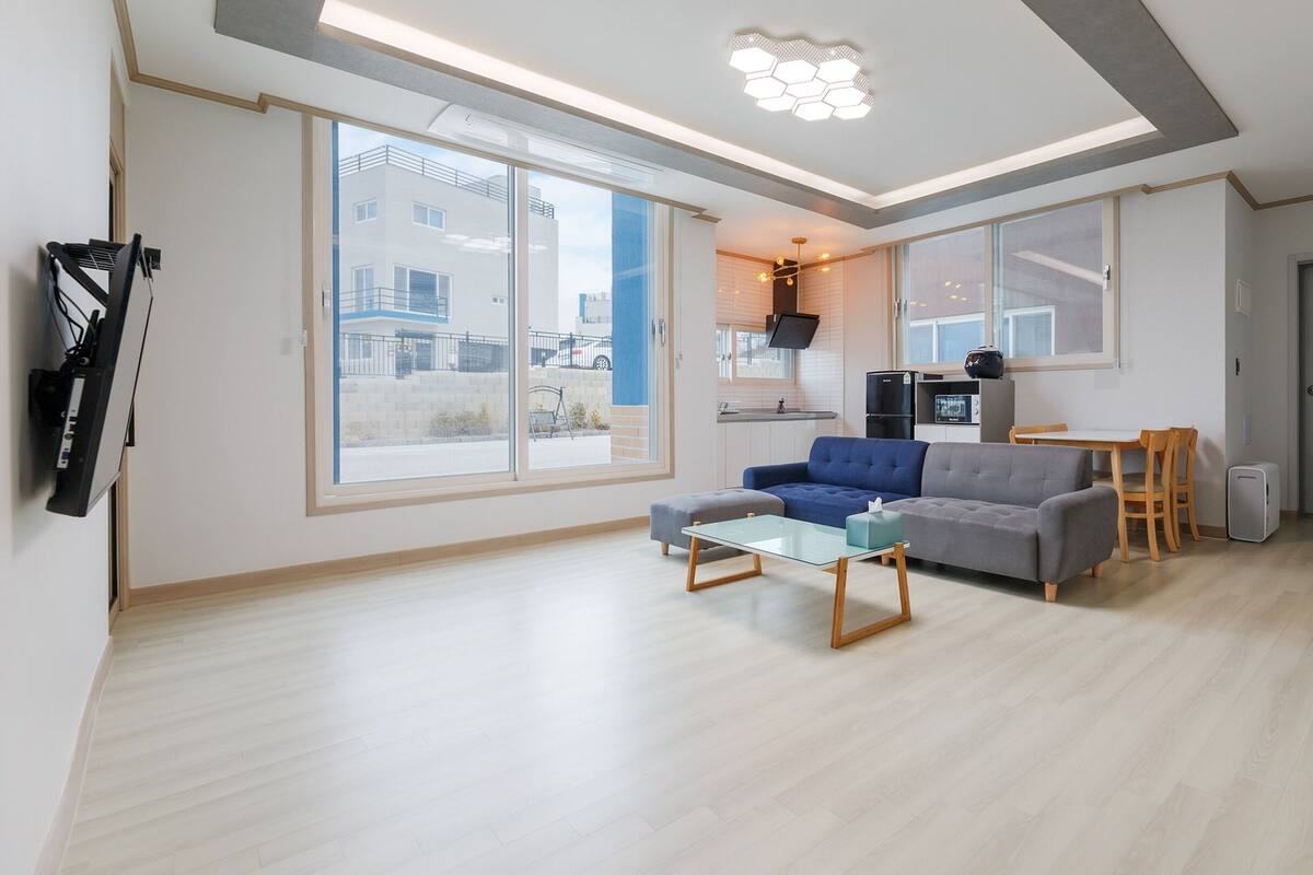 A modern living room with a sofa, a glass coffee table, and a dining area with a table and chairs.