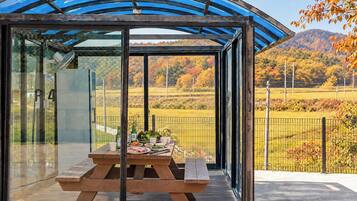 Un área de comedor al aire libre con paredes de vidrio y vistas a un paisaje campestre.