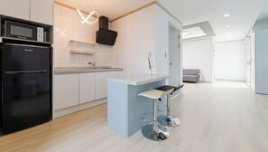 A modern kitchen with a built-in microwave, a black refrigerator, a light blue island with bar stools, and a grey sofa in the adjacent living area. - Taean Blueisland Pool Villa (Taean)