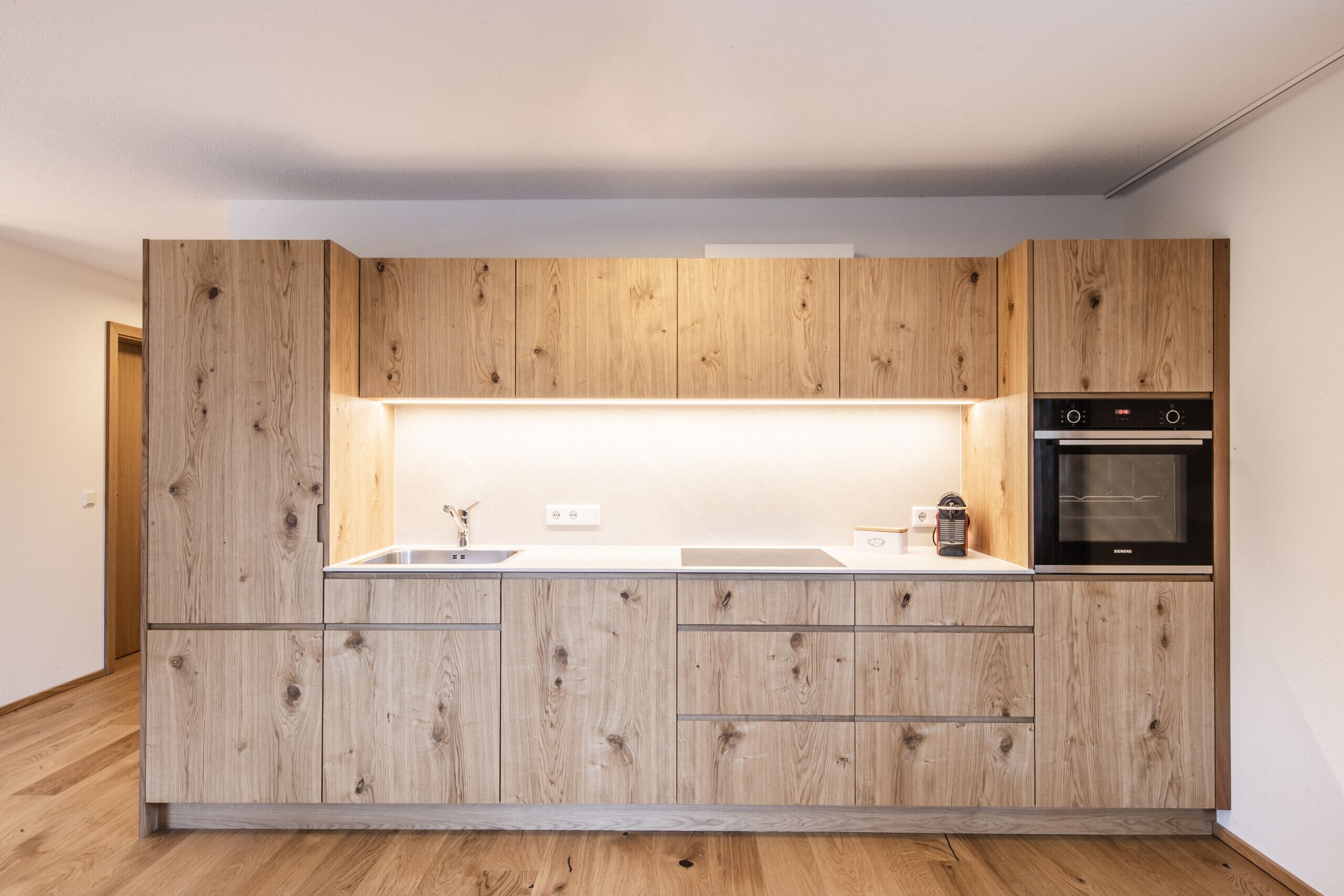 Une cuisine moderne avec des meubles en bois, un four encastré et un plan de travail doté d’un évier.