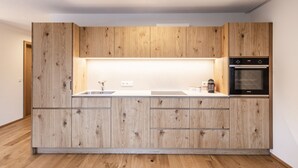 Una cuina moderna amb armaris de fusta, forn de mur i taulell amb rentatge.