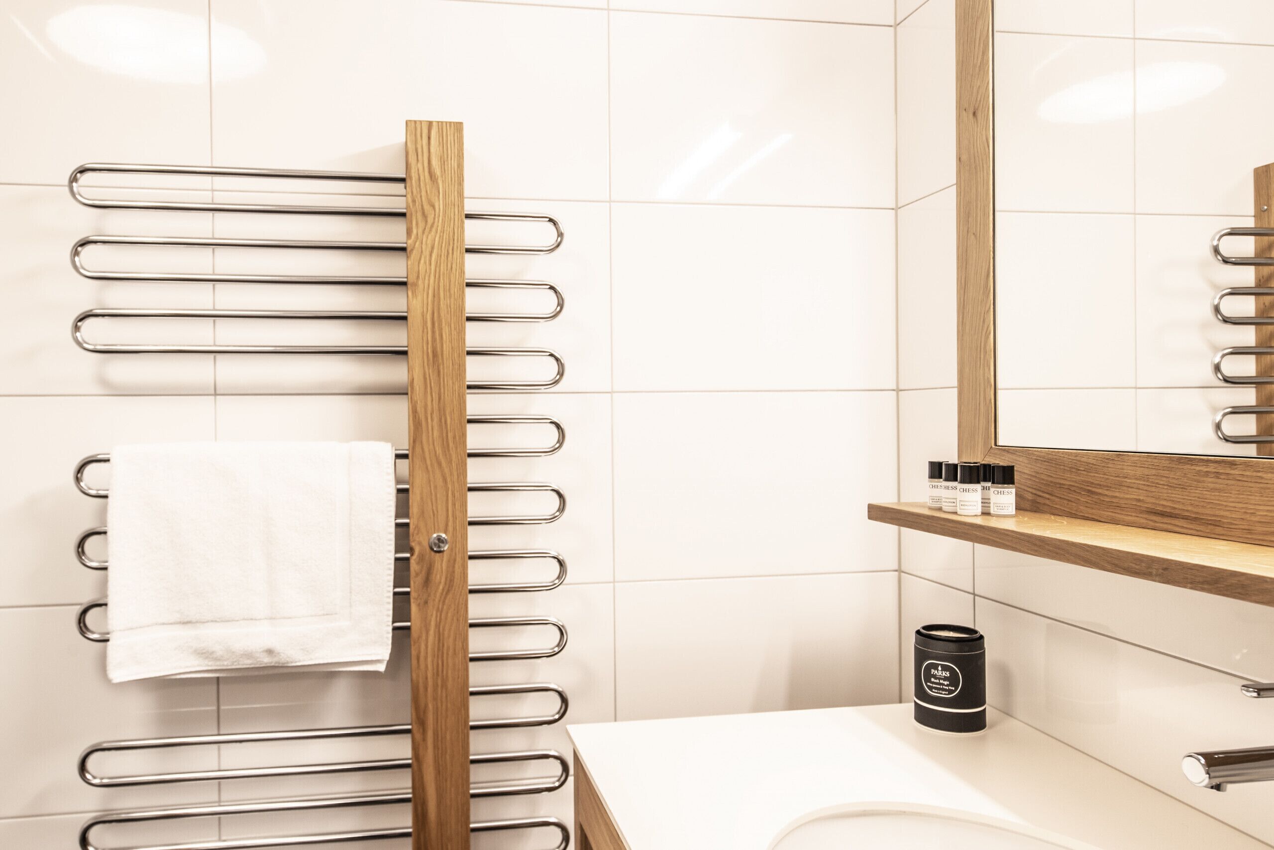 Ein Badezimmer mit einem hölzernen Handtuchhalter, einem weißen Waschbecken, einem Spiegel und einem Ablagefach mit Toilettenartikeln.