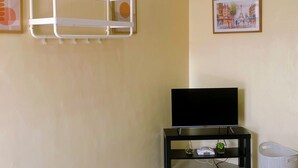 A living room with a TV on a black stand, a white shelf with hooks, a framed picture, and a white basket. - A comfy retreat in the heart of Orani, Bataan (Orani)