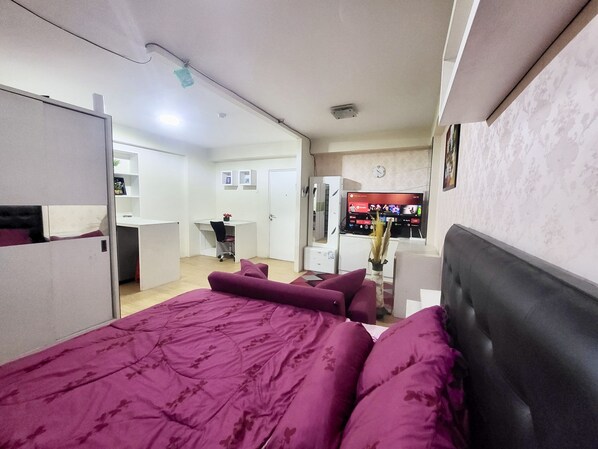 Habitación de hotel con cama, escritorio, televisión y kitchenette.