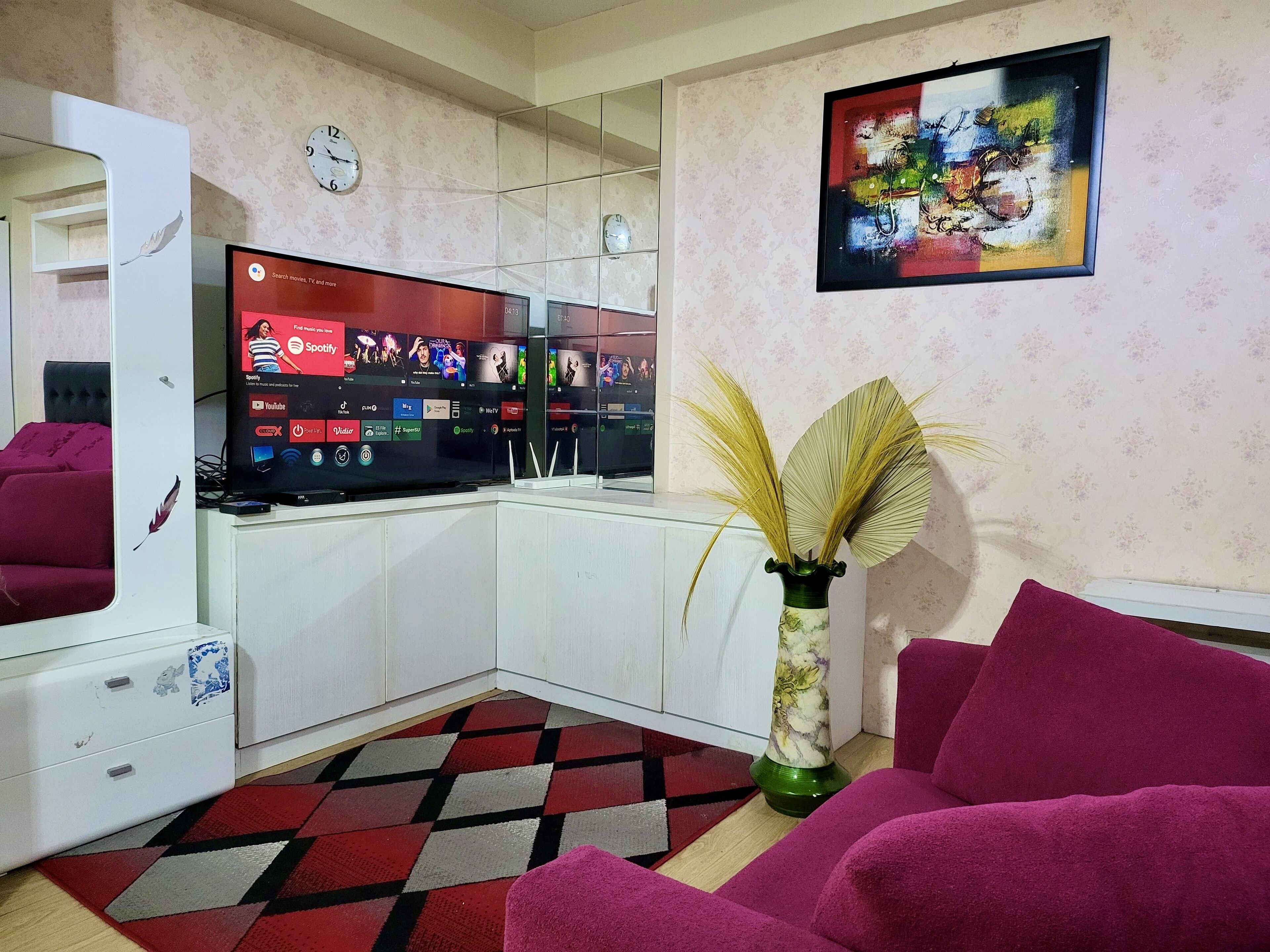 Un soggiorno con televisore a schermo piatto, un vaso decorativo e un tappeto colorato.
