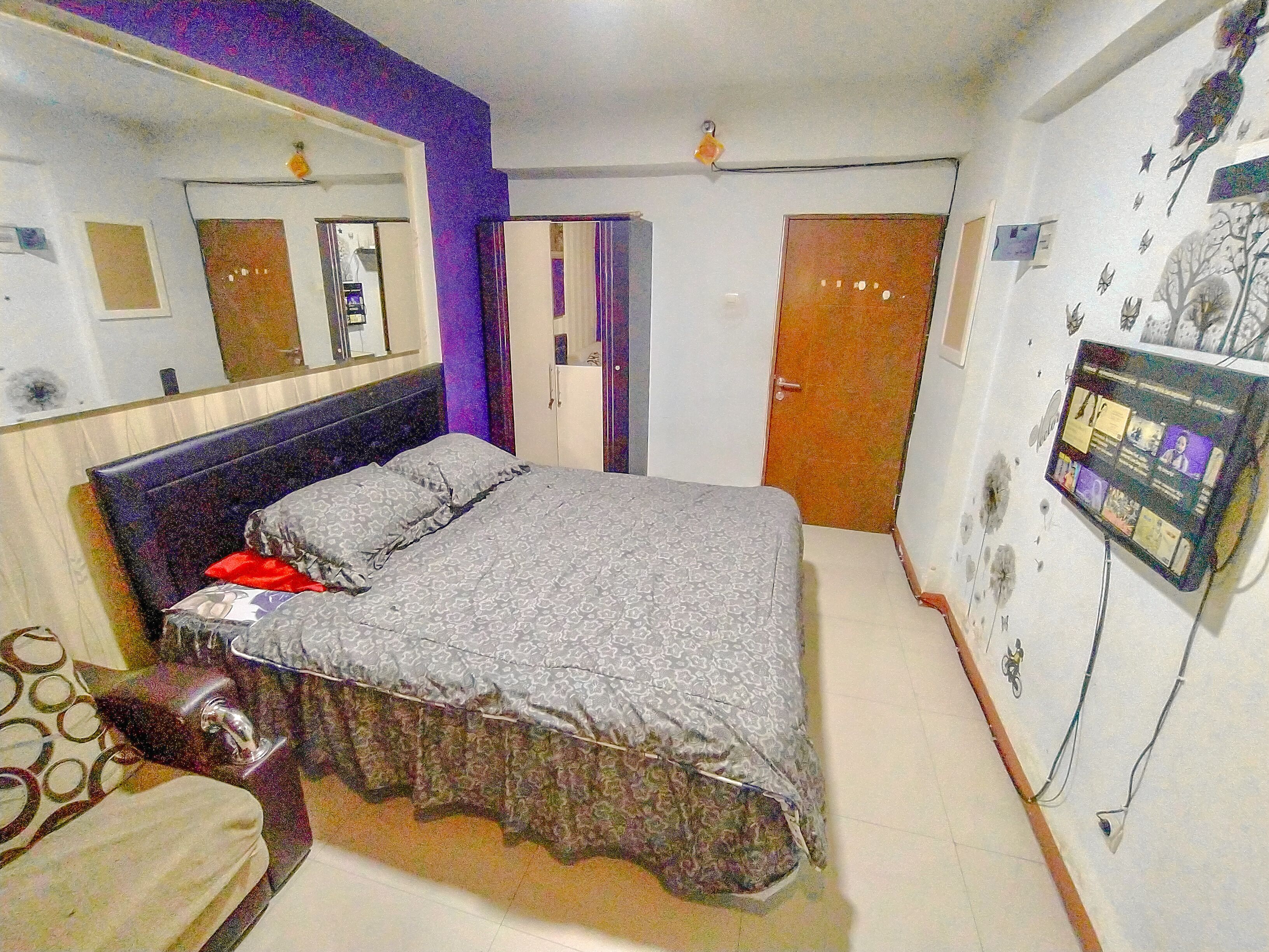 Une chambre à coucher comprenant un lit, une commode, un miroir, une armoire et un téléviseur fixé au mur.