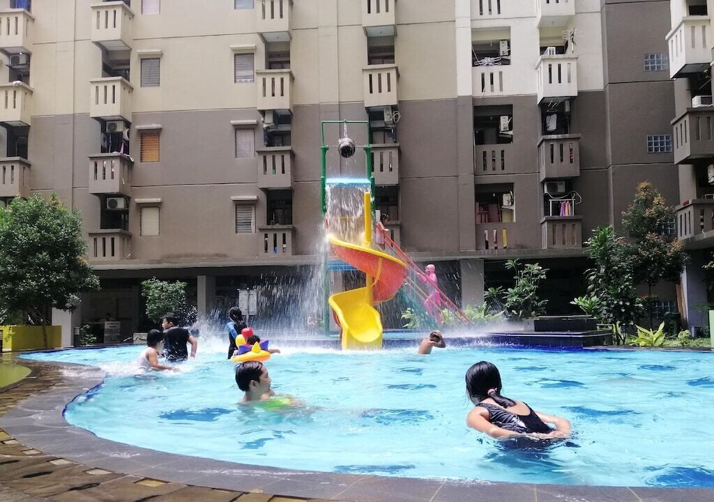 A swimming pool with a water slide, surrounded by a multi-story residential building.