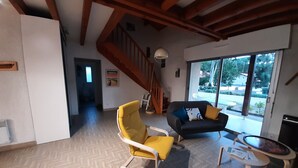 A spacious living area with a wooden staircase, a yellow armchair, a dark sofa with cushions, and a small round table.