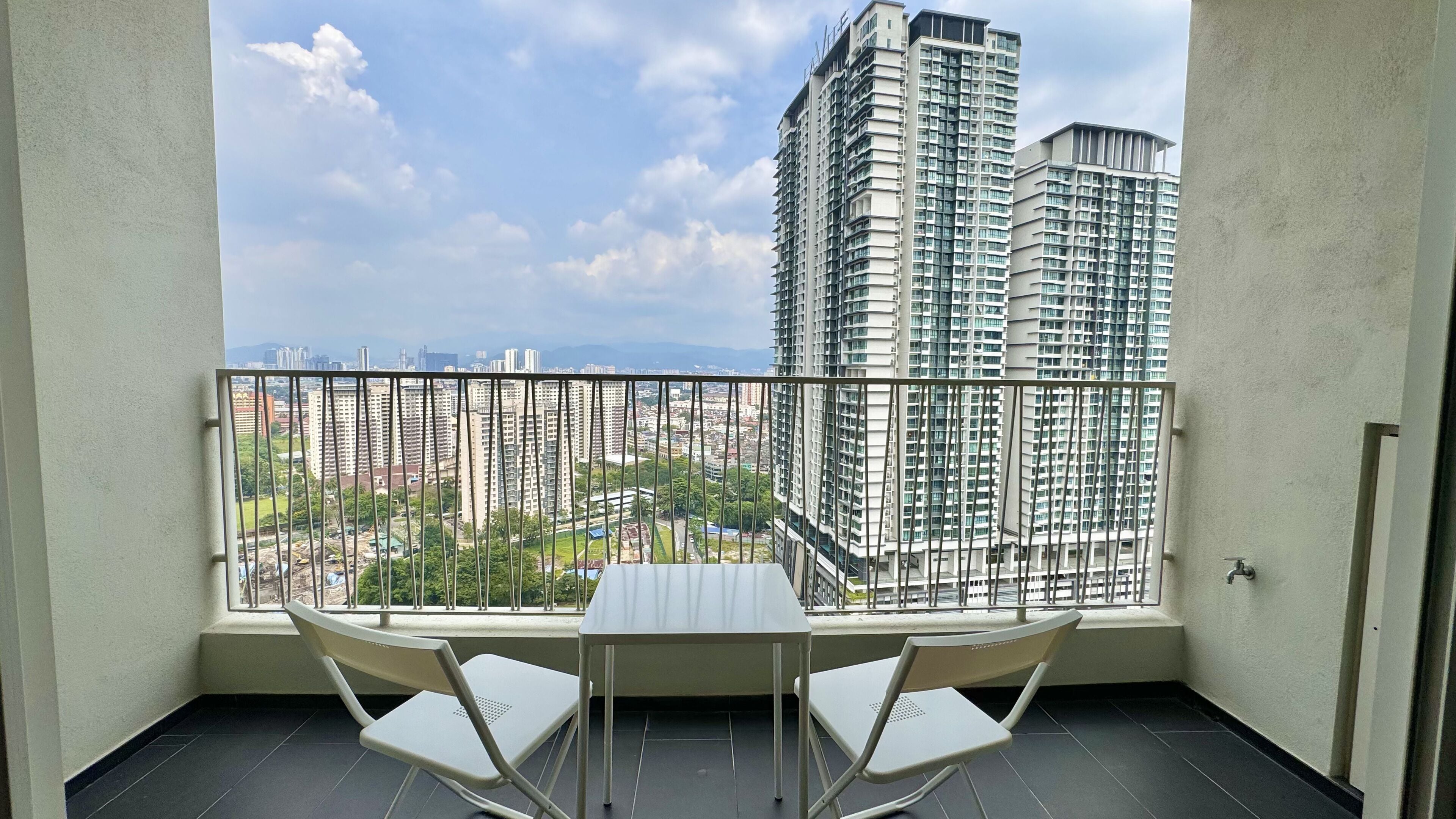 A balcony with a table and chairs, overlooking a cityscape with high-rise buildings.