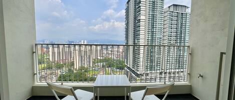 A balcony with a table and chairs, overlooking a cityscape with high-rise buildings.