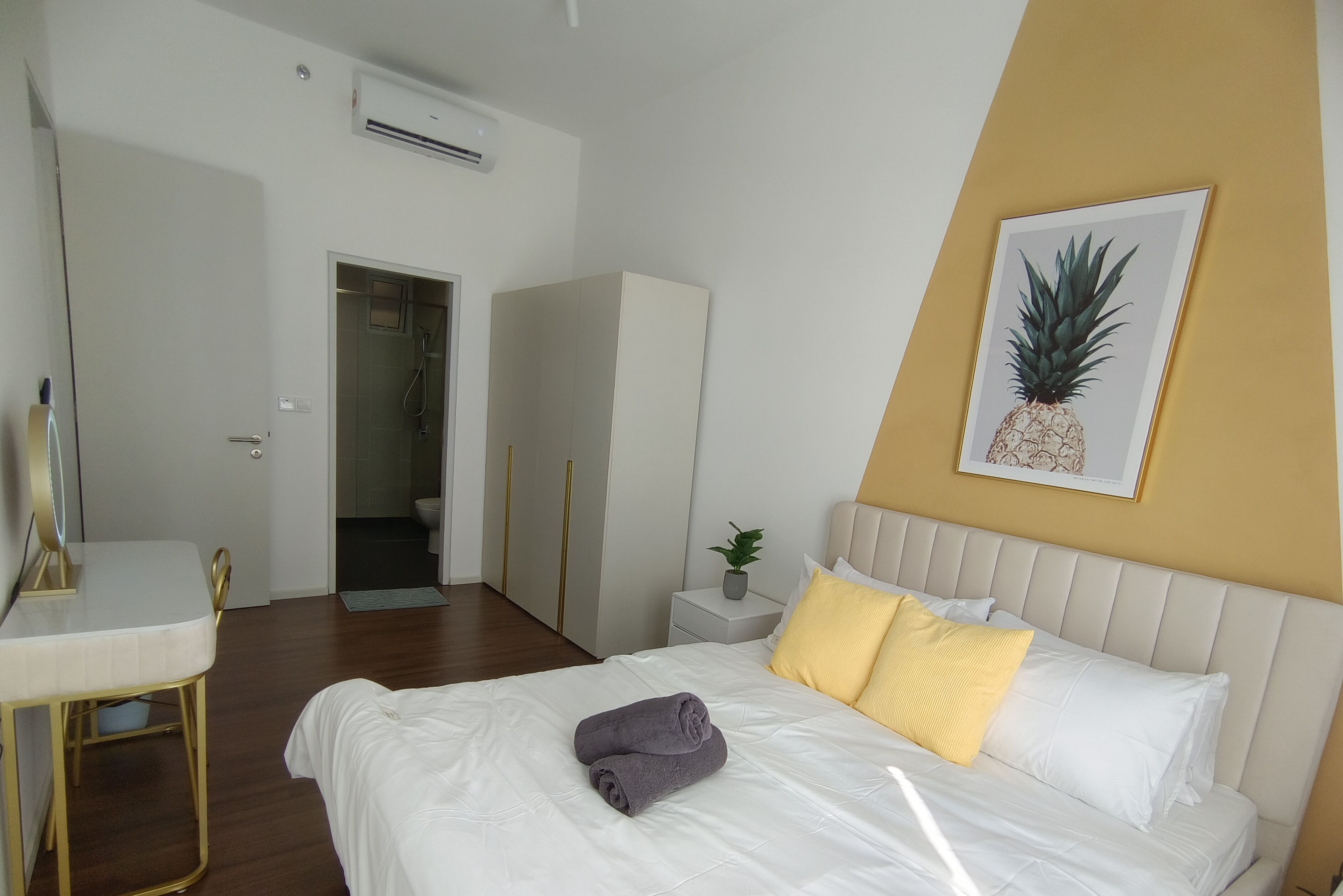 A hotel room with a bed, a bedside table, a small potted plant, and a framed pineapple artwork on the wall.