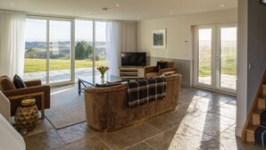 A spacious living room with a large sofa, a television, and a view of the outdoors. - Robin Cottage, Logiealmond Estate (Perth)