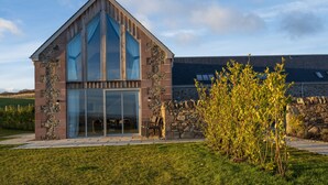 A modern house with a stone facade, large glass windows, and a stone wall. - Robin Cottage, Logiealmond Estate (Perth)