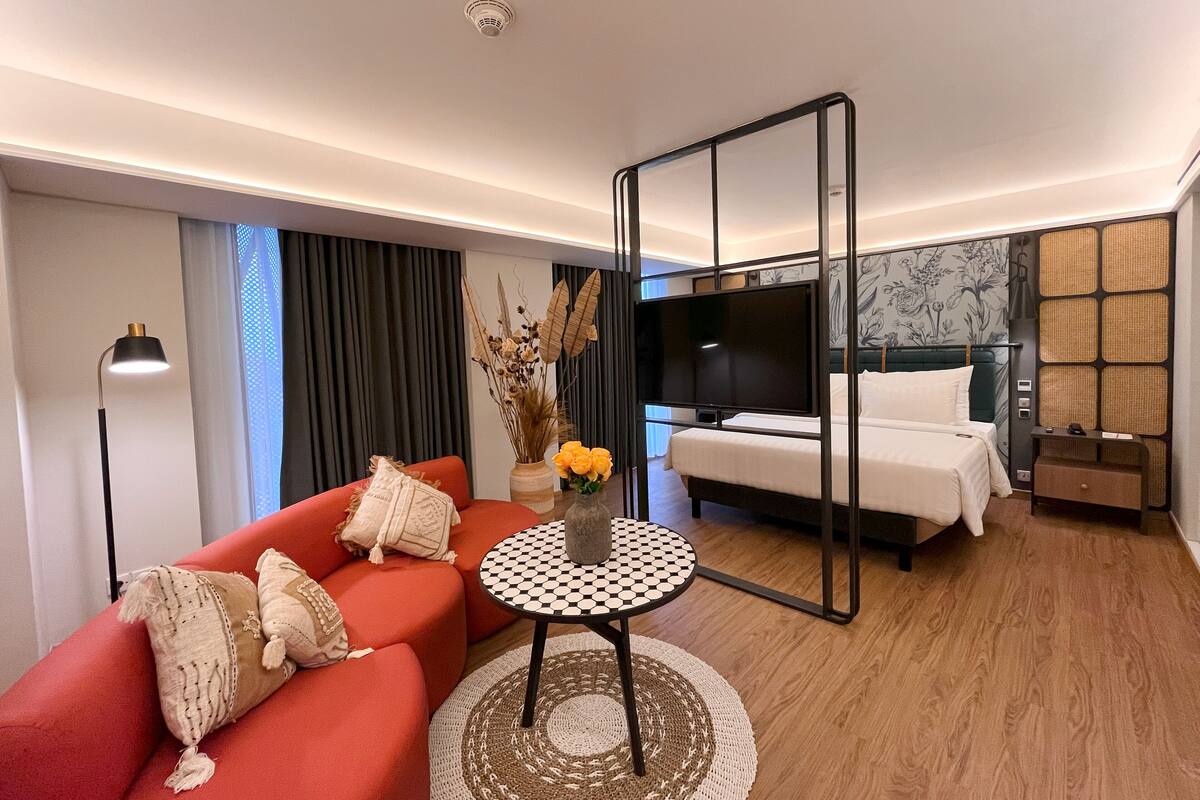 A modern hotel room with a red sofa, a round table, a bed with white bedding, and a large mirror.