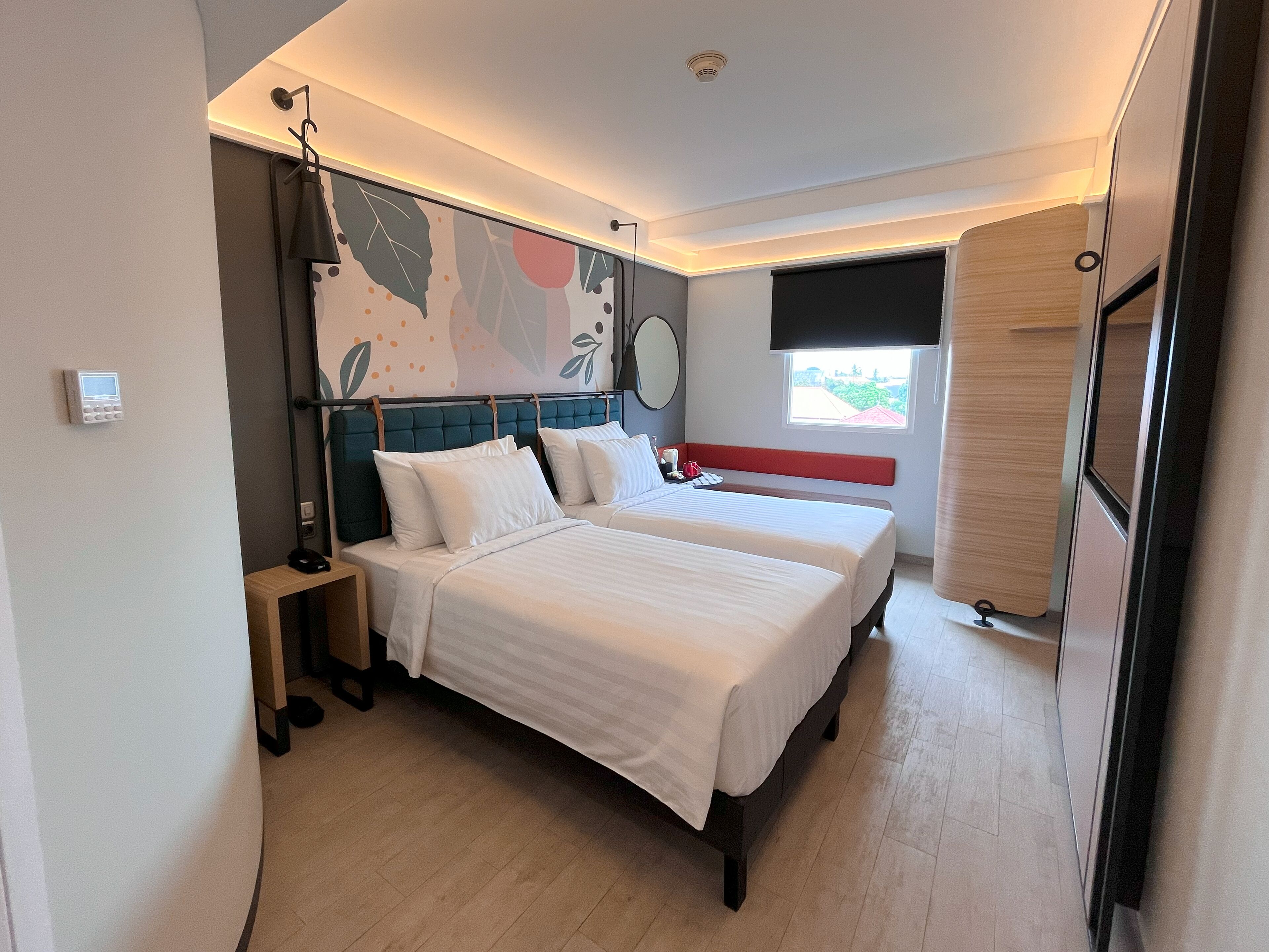 Ein modernes Hotelzimmer mit zwei Betten, einem Nachttisch, einer Lampe und einem Fenster mit Blick.