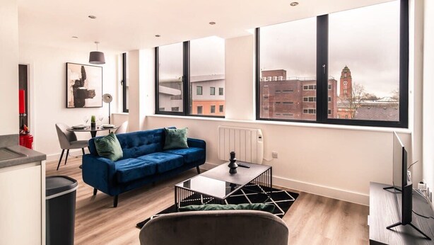 En moderne lejlighed med en blå sofa, et spisebord og et stort vindue med udsigt over byen.