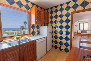 A kitchen with a view of the sea, a refrigerator, a sink, and wooden cabinets.