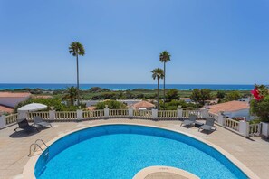 A swimming pool with a view of the ocean, surrounded by palm trees and a white fence.