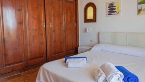 A hotel room with a large wooden wardrobe, a bed with white linens, and a small bedside table with a lamp. - Villa Bautista - Beautiful Sea View (San Jaime Mediterráneo)