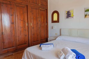 A hotel room with a large wooden wardrobe, a bed with white linens, and a small bedside table with a lamp.