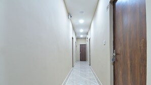 A narrow, well-lit hallway with a marble floor, wooden doors, and a ceiling light fixture. - Chowdhry Tourist Lodge- Paharganj-NDLS (New Delhi)