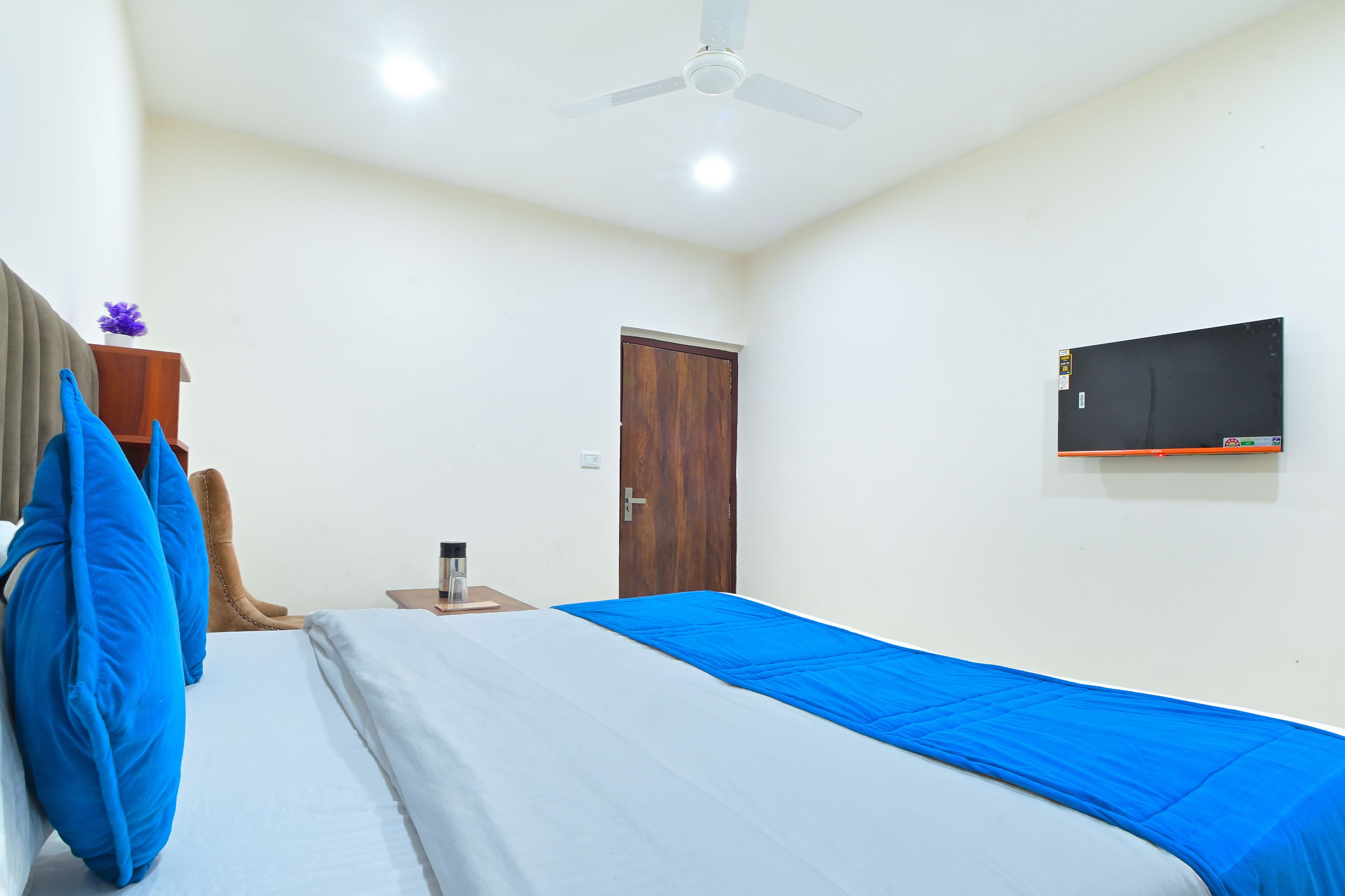 Una camera da letto con un letto, un armadio in legno, un comodino con una lampada, una ventola a soffitto e una TV a parete.