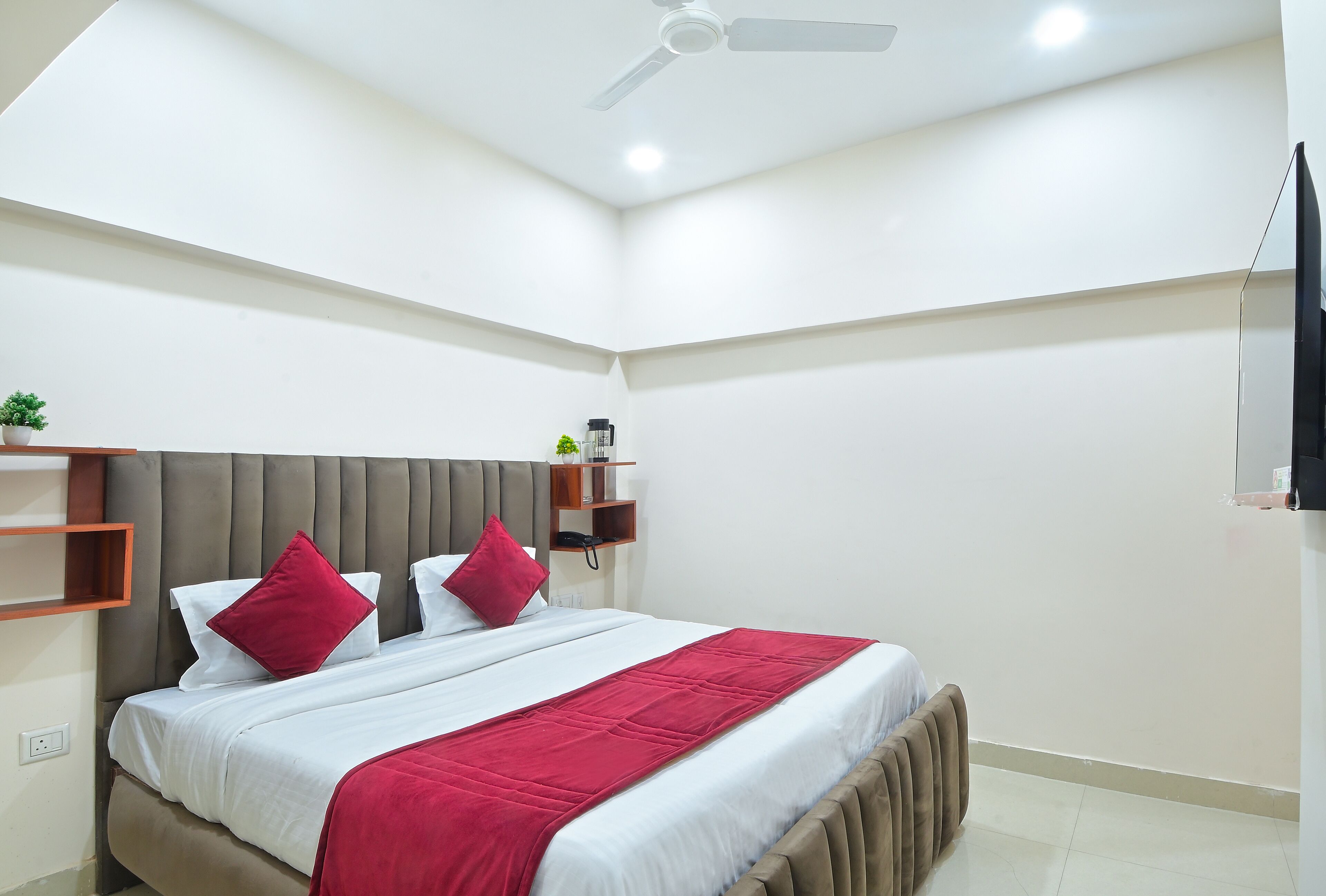 Ein modernes Hotelzimmer mit Bett, Deckenventilator, kleiner Pflanze und Ablagefläche mit Telefon und Kaffeemaschine.
