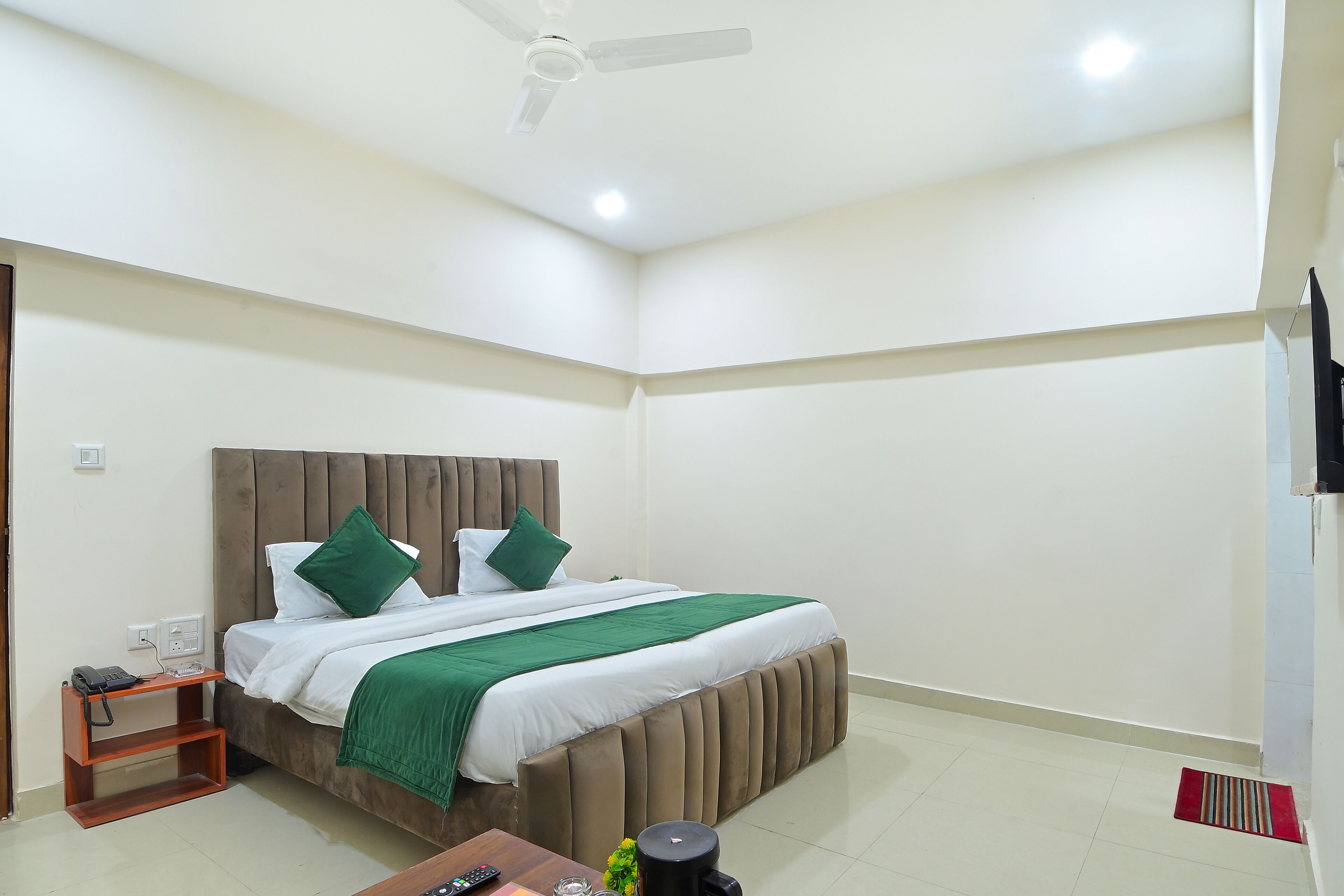 Habitación de hotel ordenada con cama, mesita de noche y ventilador de techo.
