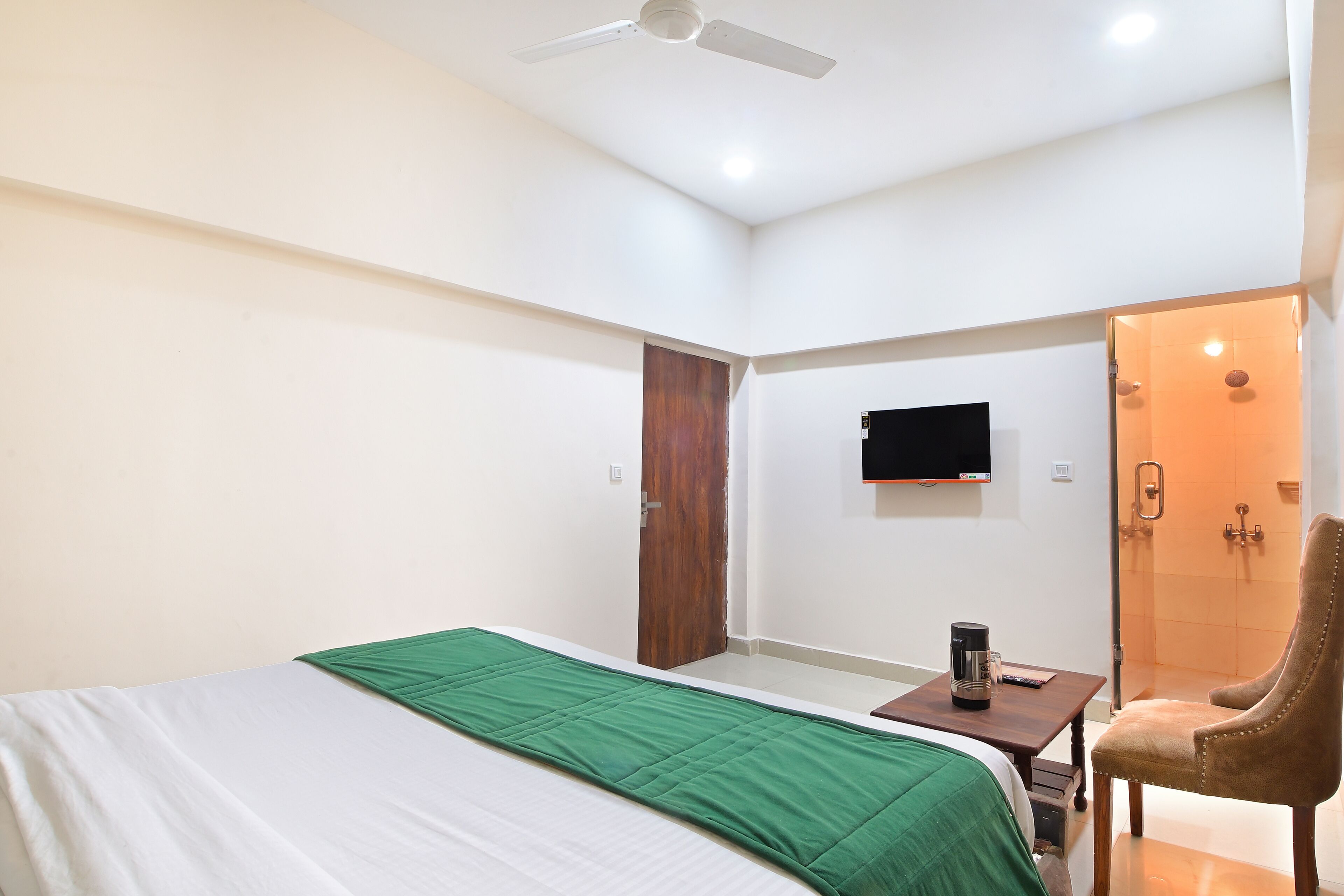 A hotel room with a bed, a desk with a coffee maker, a TV mounted on the wall, and a shower area.