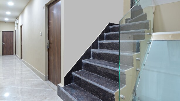A hallway with a marble floor, a wooden door, and a glass railing staircase. - Chowdhry Tourist Lodge- Paharganj-NDLS (New Delhi)