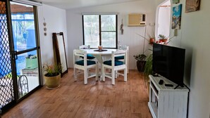 A dining area with a white table and chairs, a television, and potted plants.