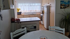 A compact kitchen with a white refrigerator, stove, and microwave. There is a small dining table with two chairs.