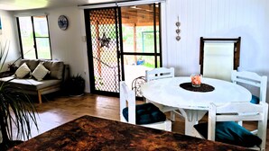 A cozy room with a white sofa, a dining table with chairs, and a large window with a view of the outdoors.