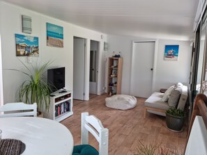 A living room with a white sofa, a TV on a white stand, a bookshelf, and a potted plant. - Cosy 2 bedroom cabin, with private fully fenced yard and alfresco area.  (Pillar Valley)