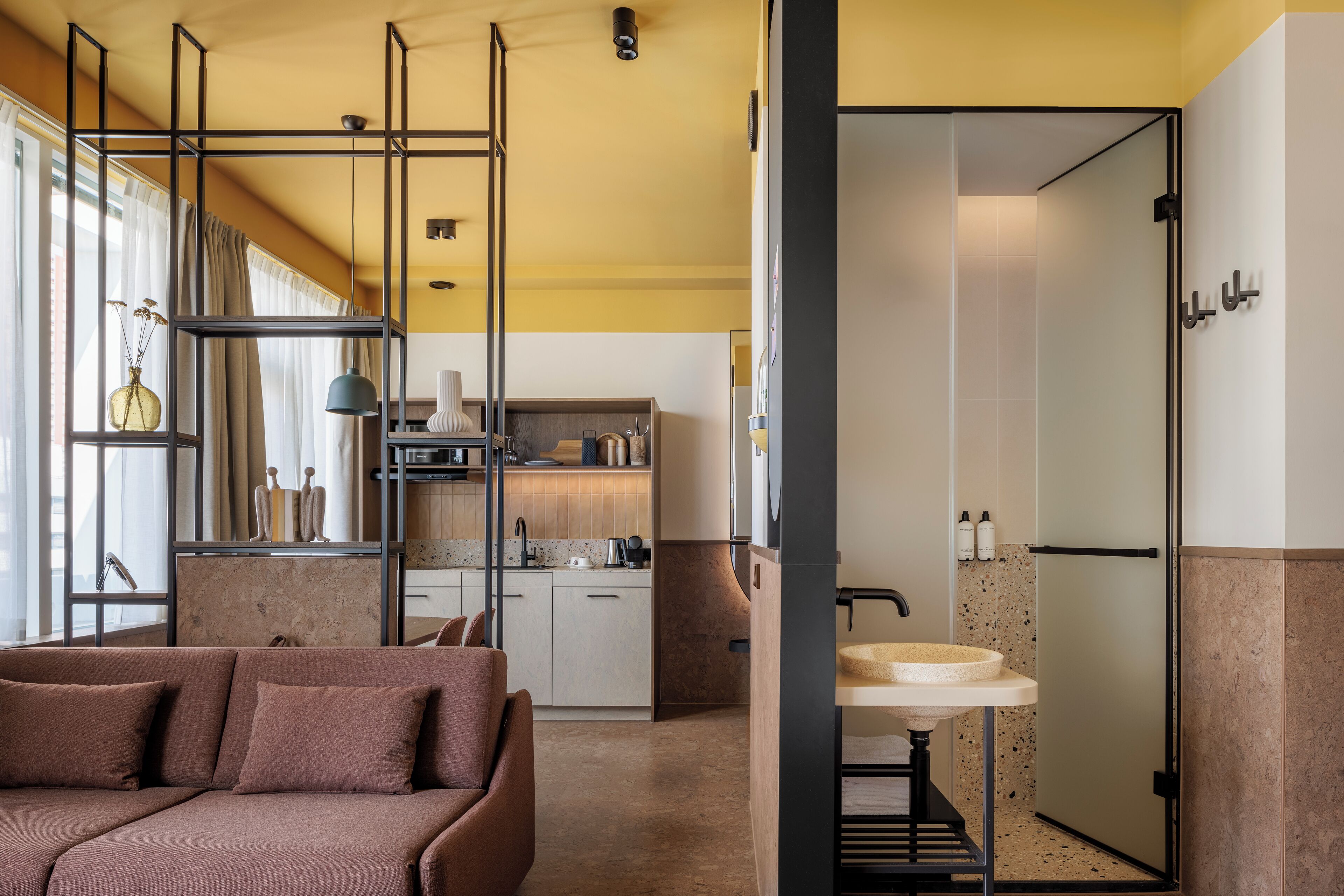 A modern living room with a sofa, a kitchen in the background, and a bathroom with a sink and shower.