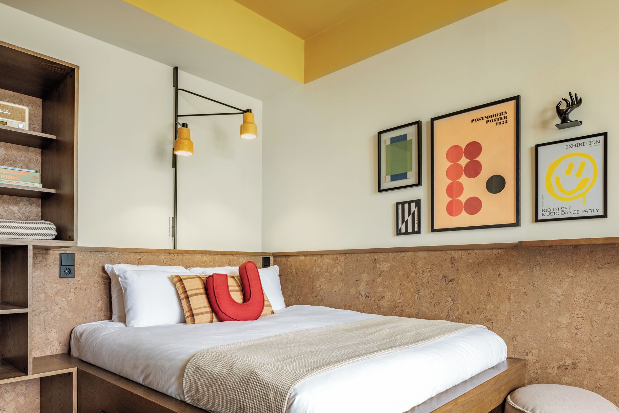 Een moderne slaapkamer met een bed, een hoofdeinde, een plank met boeken en wanddecoratie.